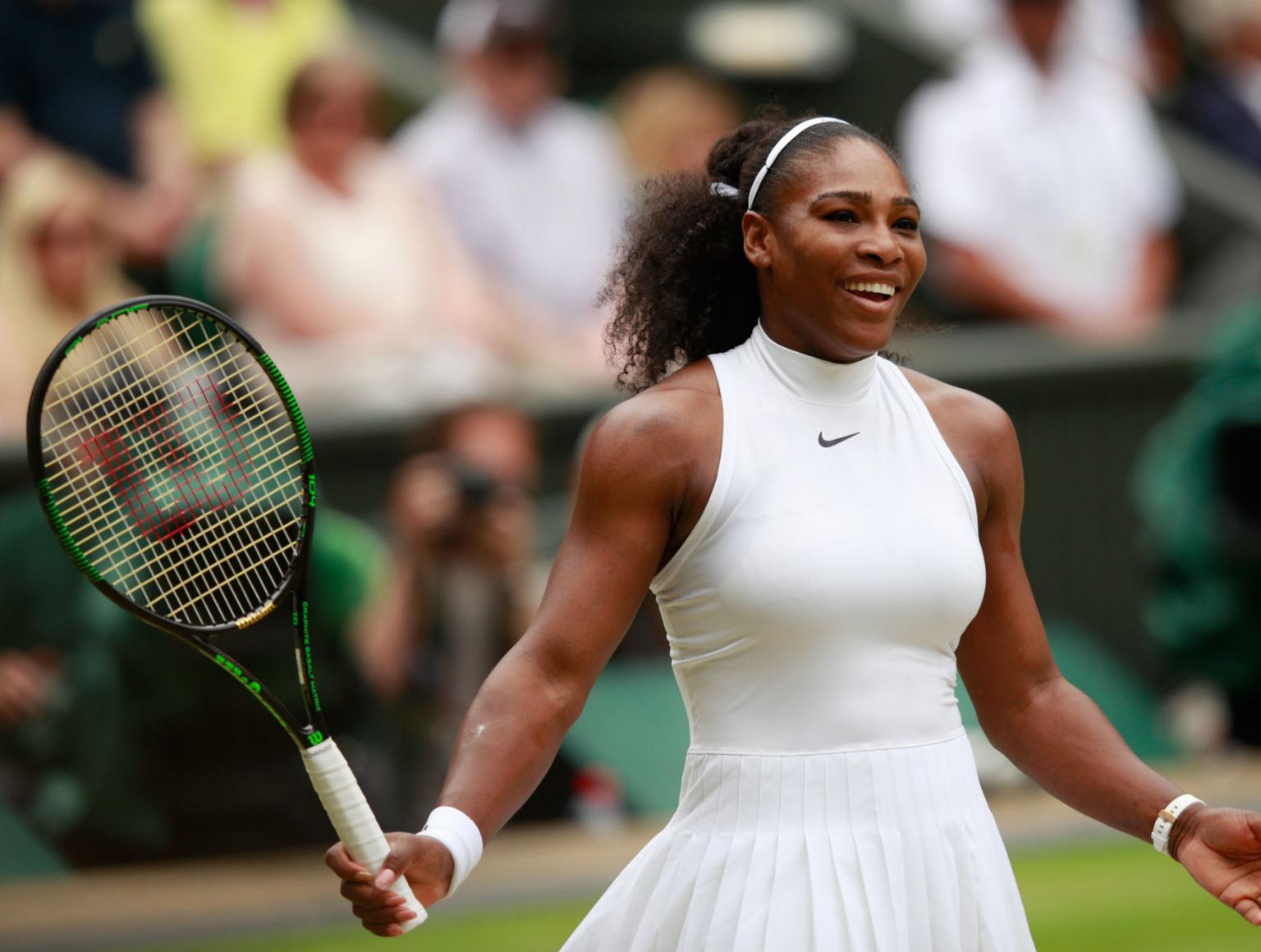 Serena Williams dressed in Nike logo white athletic top and white skirt, holding a tennis racket. Action shot